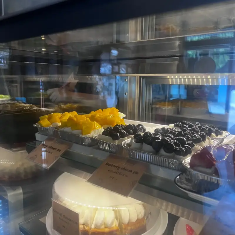 ขนมหวานชิ้นเล็กหน้าผลไม้สีเหลืองและเบอร์รี่สีเข้ม วางอยู่เหนือเค้กทั้งก้อน