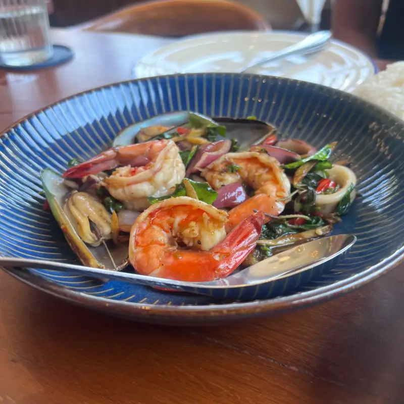 A dish with prawns, mussels and vegetables on a blue plate