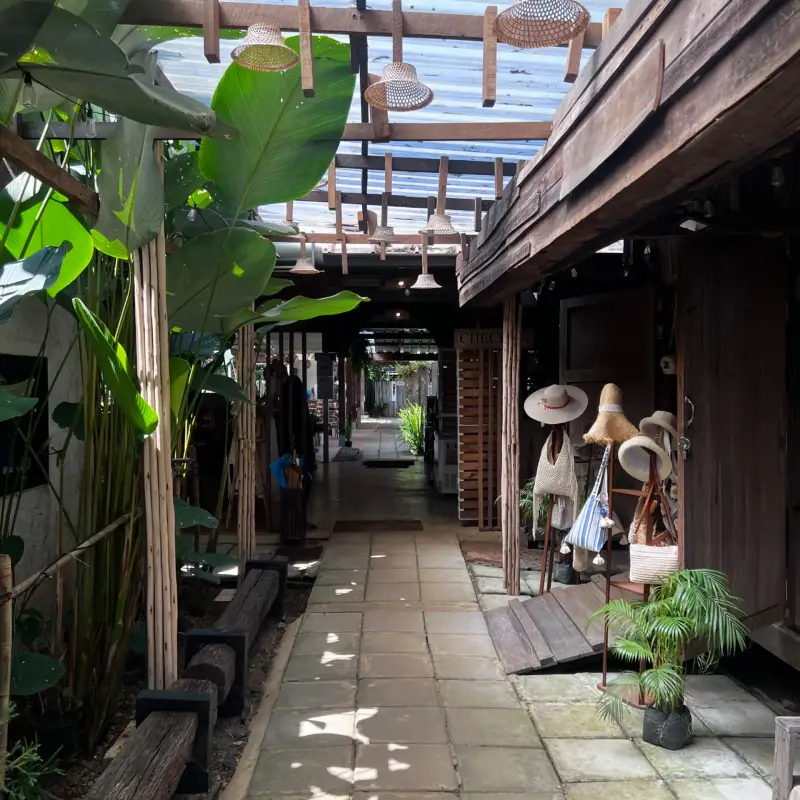 Covered walkway between wooden façades, plants and clothing displays