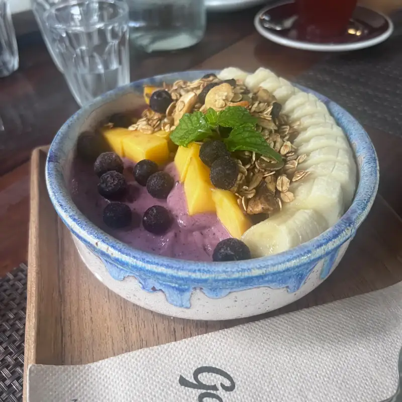 Bowl mit Bananenscheiben, Beeren, gelben Fruchtstücken und Müsli
