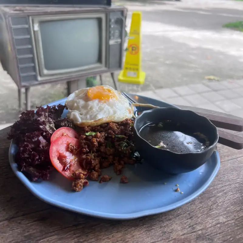 Teller mit Spiegelei und Salat auf einem Holztisch vor einem alten Fernseher
