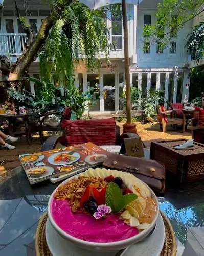 Pinkfarbene Bowl mit Obst auf einem Tisch im begrünten Innenhof