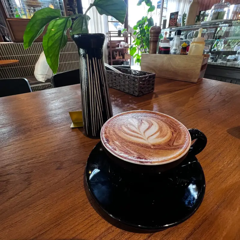 Kaffee mit blattförmiger Latte Art neben einer schlanken Vase